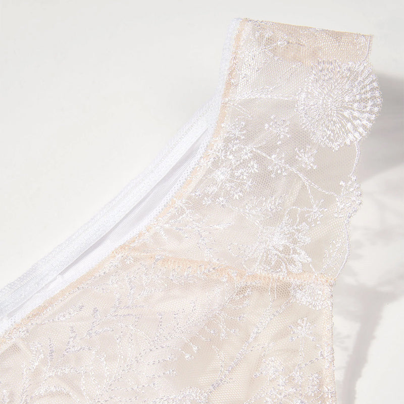 close-up of a beige lace garment with floral embroidery on a white background