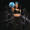 woman in athletic wear holding a blue medicine ball against a dark background