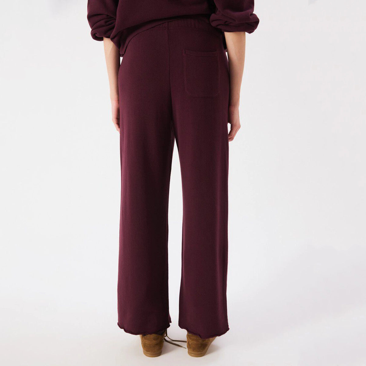 A person shown from the back wearing loose, wide-leg trousers in a deep burgundy or plum tone, paired with a matching top and tan shoes, against a plain light background.