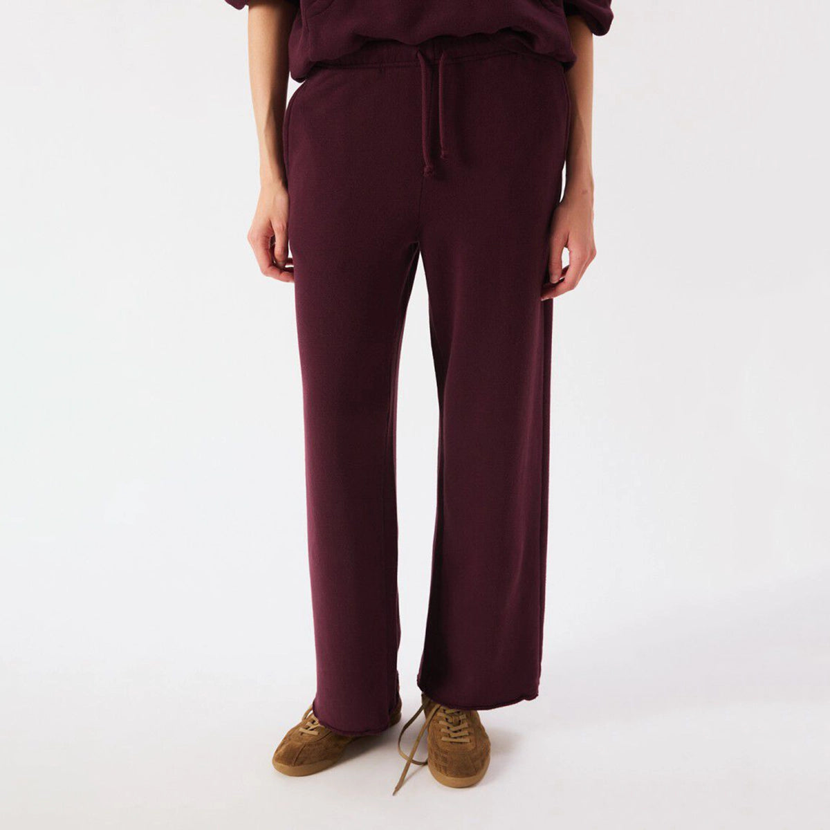 A person wearing loose, wide-leg drawstring sweatpants in a deep burgundy/plum shade, paired with brown suede shoes, photographed against a clean white studio background.