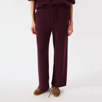 A person wearing loose, wide-leg drawstring sweatpants in a deep burgundy/plum shade, paired with brown suede shoes, photographed against a clean white studio background.