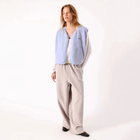 A woman modeling a light blue vest over a white top and beige wide-leg trousers, standing against a plain white studio background.