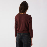 A woman viewed from behind wearing a dark burgundy long-sleeve knit top and dark blue jeans against a plain white studio background.