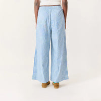 A person shown from the back wearing light blue and white gingham wide-leg pants, paired with a white top and brown wedge sandals, against a plain off-white studio background.