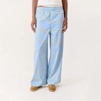 A person wearing light blue and white gingham wide-leg pants, paired with a white cropped top and tan shoes, standing against a plain off-white studio background.