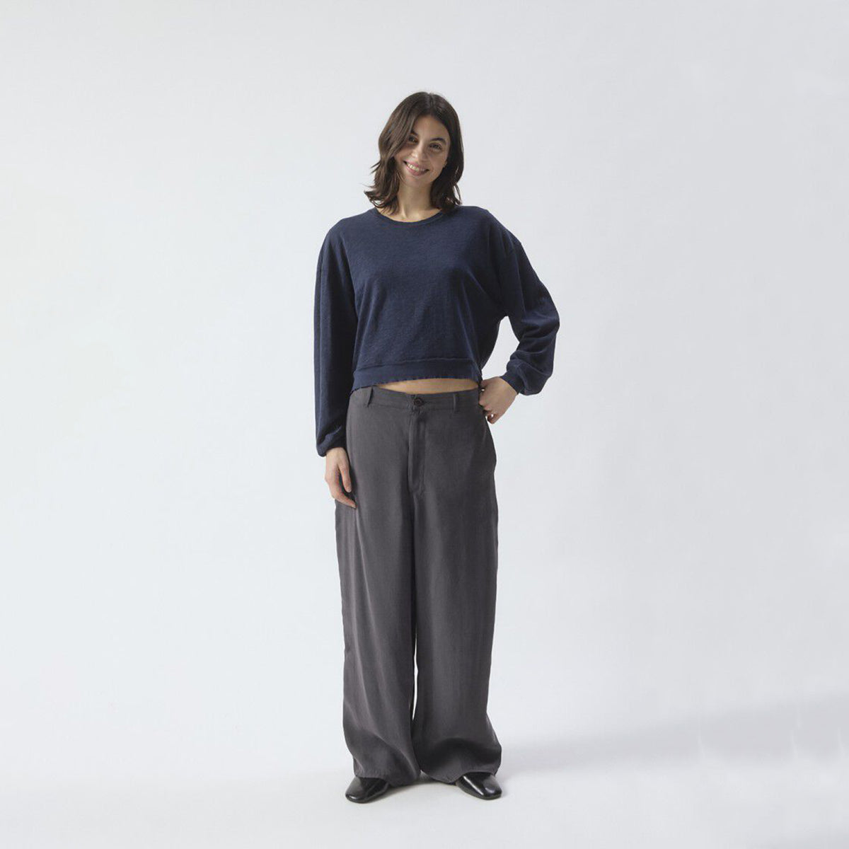 A woman modeling a dark navy blue long-sleeve top and dark gray wide-leg trousers against a plain white studio background.