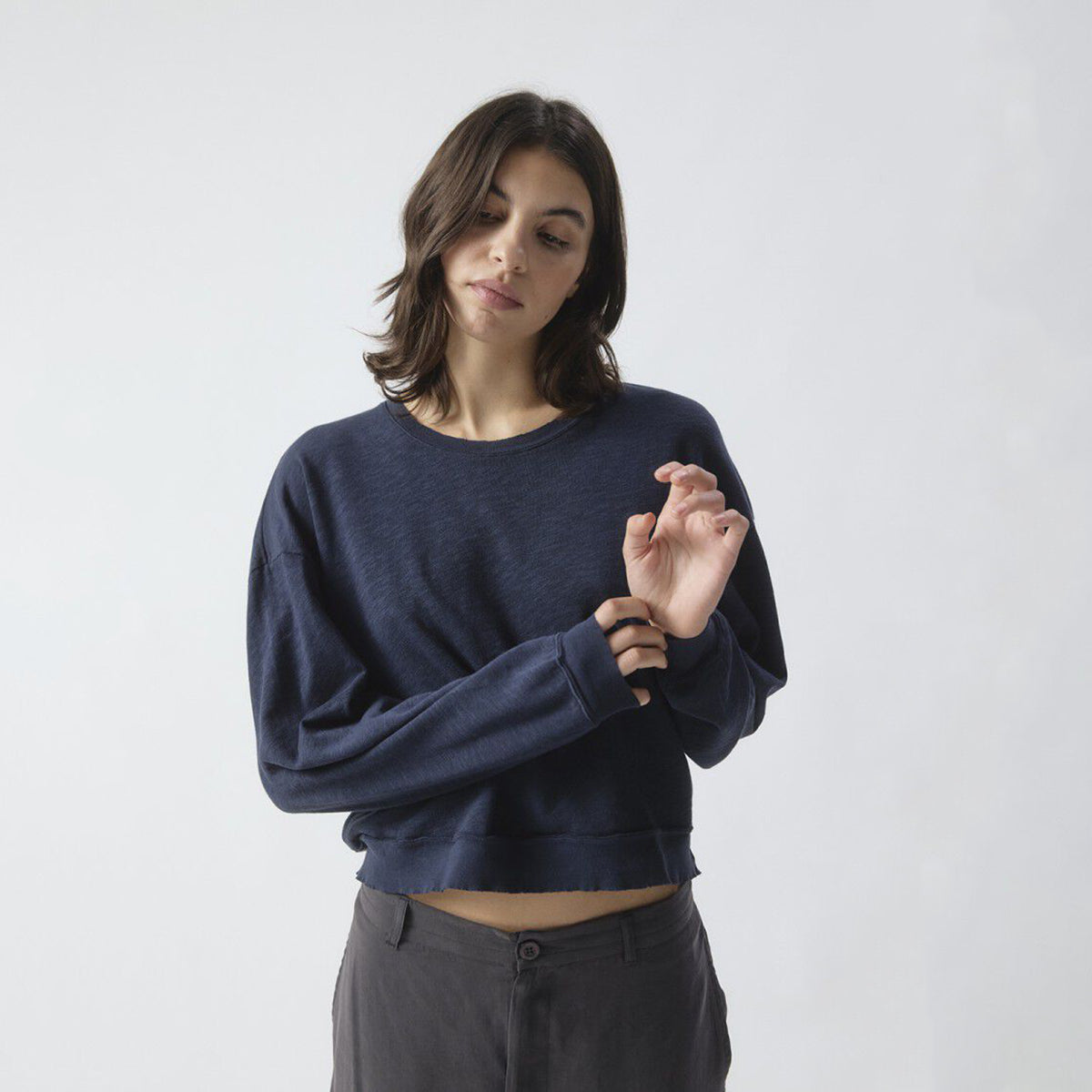 A woman wearing a dark navy blue long-sleeve sweatshirt and dark gray pants, standing against a light gray studio background.