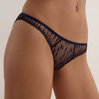 Cut out of a woman wearing a navy blue brief with gold-tone detail and sheer patterned mesh, photographed against a plain light beige studio background.