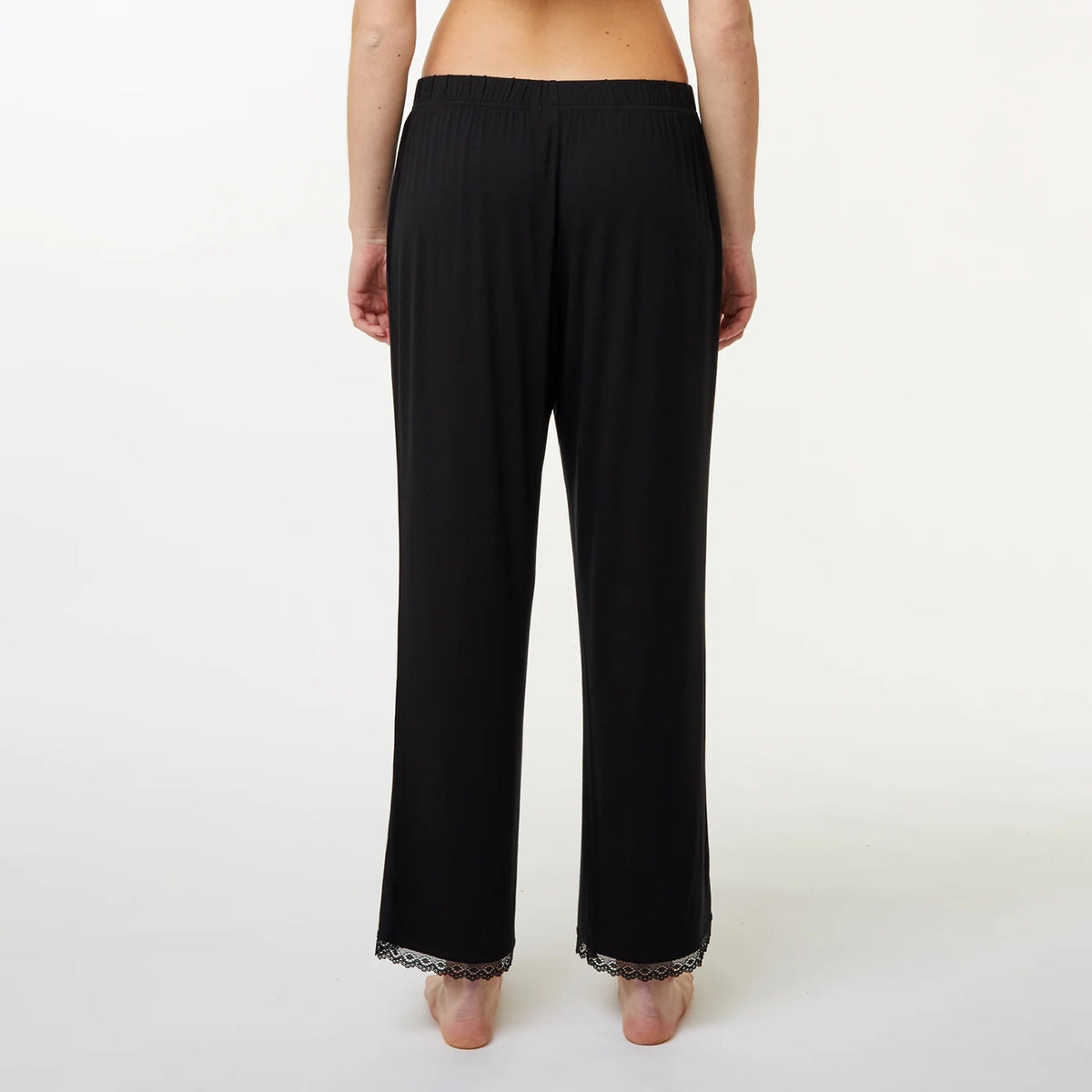 A model shown from the back wearing black wide-leg lounge pants with a lace trim at the hem, against a plain white studio background.