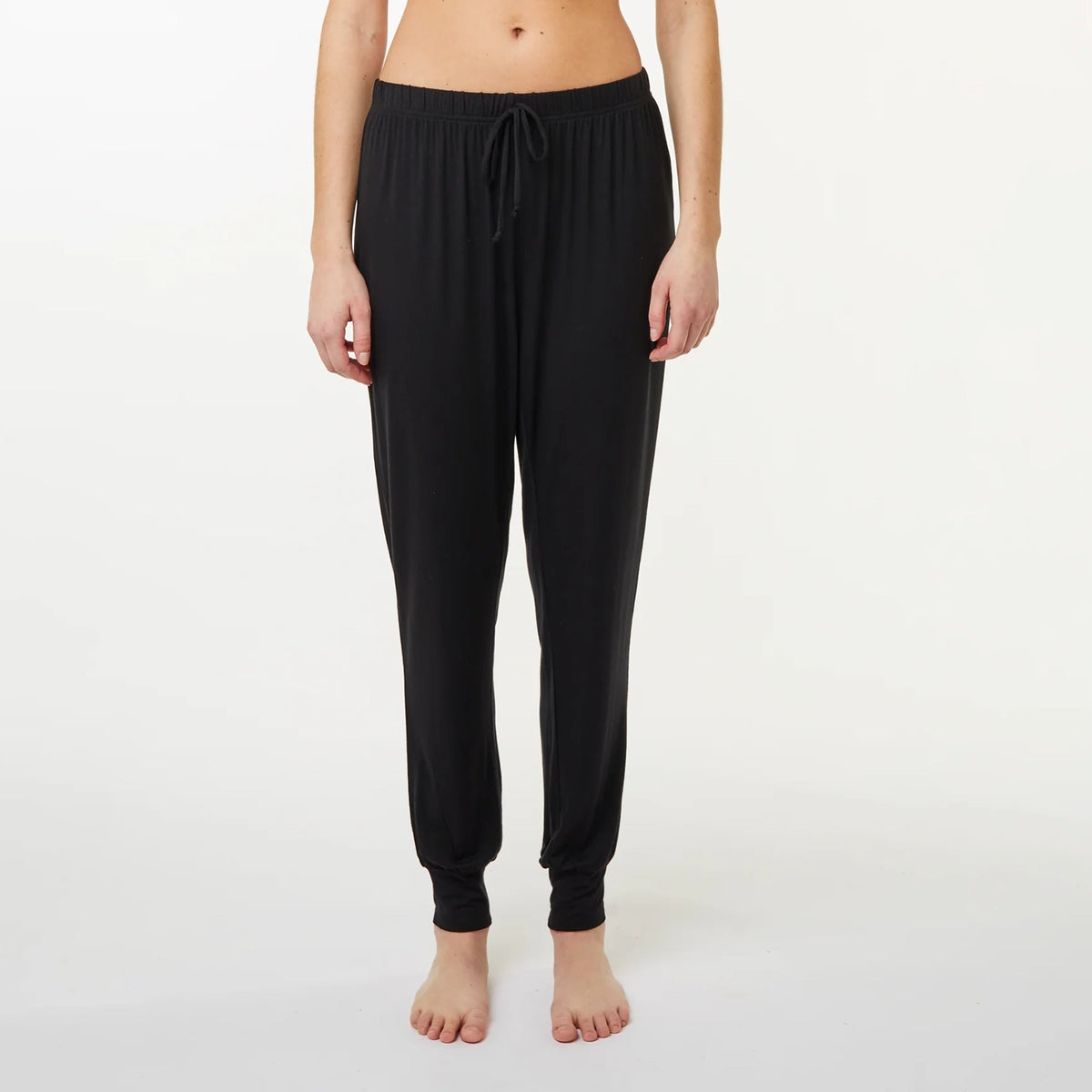A model wearing black jogger-style pyjama pants with a drawstring waist and elastic ankle cuffs, shown against a plain light gray studio background.