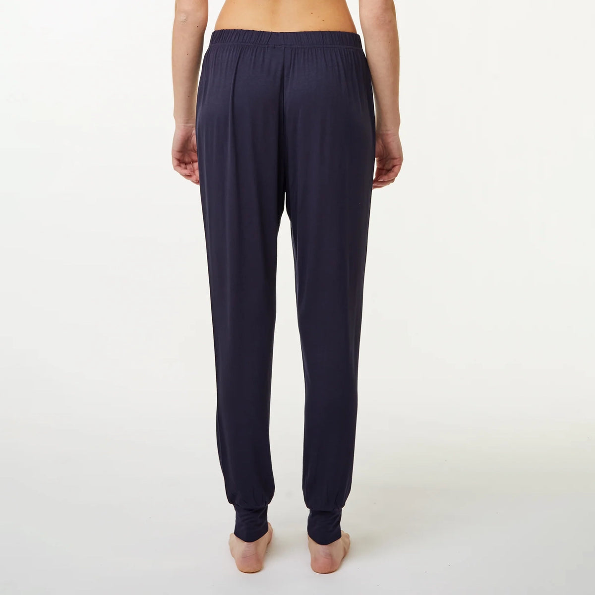 A person shown from the back wearing dark navy jogger-style pyjama bottoms with an elastic waistband and ribbed ankle cuffs, standing against a plain light background.