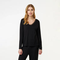A woman modeling a black long-sleeve top with a scalloped lace V-neckline, paired with black pants, against a plain white studio background.