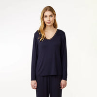 A woman modeling a navy blue long-sleeve top with a scalloped lace V-neckline, paired with matching navy pants, against a plain white studio background.