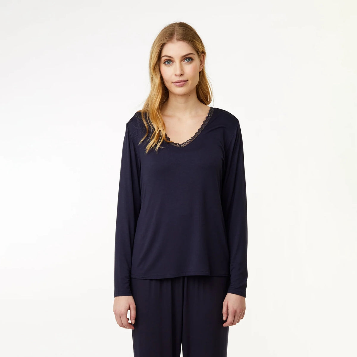 A woman modeling a navy blue long-sleeve top with a scalloped lace V-neckline, paired with matching navy pants, against a plain white studio background.