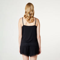 A woman viewed from the back wearing a black camisole top with thin straps and matching black shorts with lace trim, against a plain light background.