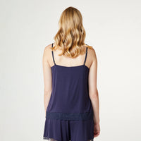 A woman viewed from the back wearing a navy blue camisole and matching shorts set, photographed against a plain light gray studio background.
