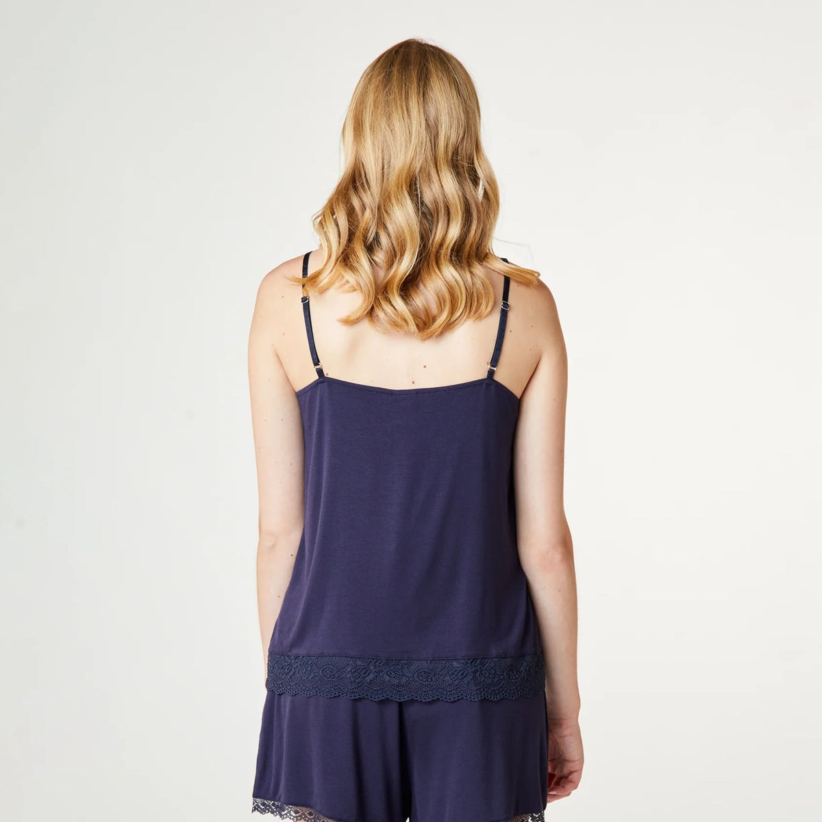 A woman viewed from the back wearing a navy blue camisole and matching shorts set, photographed against a plain light gray studio background.