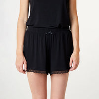 A person wearing black lounge shorts with a lace hem and a small bow at the elastic waistband, paired with a matching top against a light studio background.