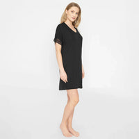 A woman modeling a black short-sleeve nightgown with black lace trim on the sleeves, standing against a plain white studio background.
