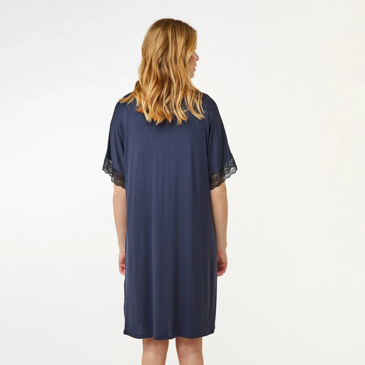 A woman viewed from the back wearing a navy blue short-sleeve nightgown with black lace trim at the sleeve cuffs, set against a plain white studio background.
