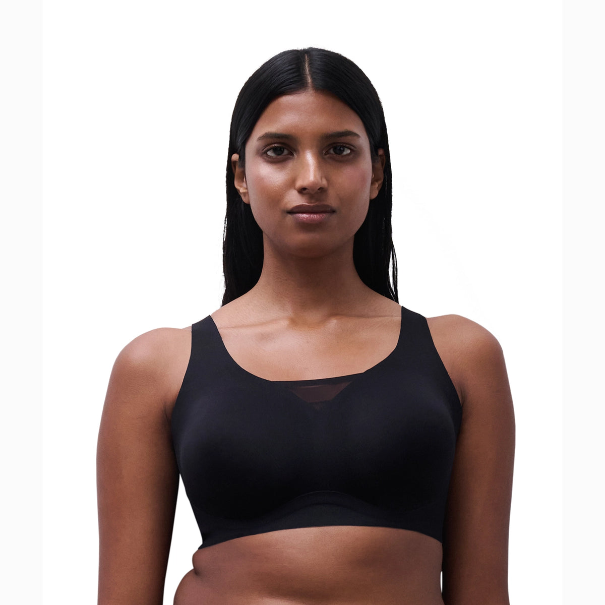 A woman with long, straight black hair wearing a black wireless bralette with a scoop neckline and a subtle sheer mesh panel at the center front, set against a plain white background.
