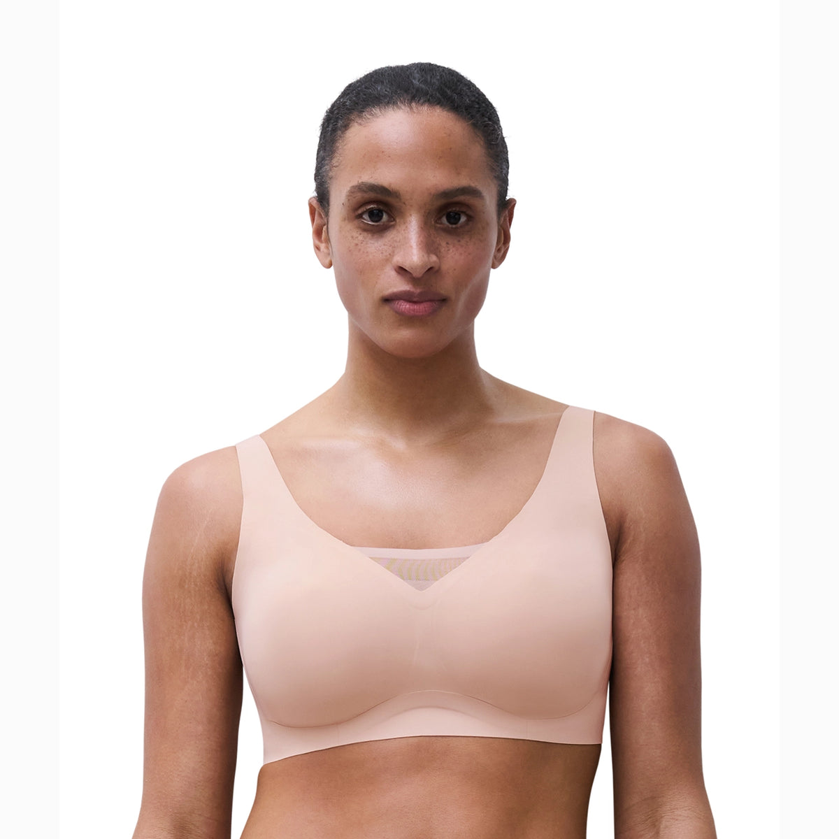 A woman modeling a seamless, light peach-beige underwire bra against a plain white background.