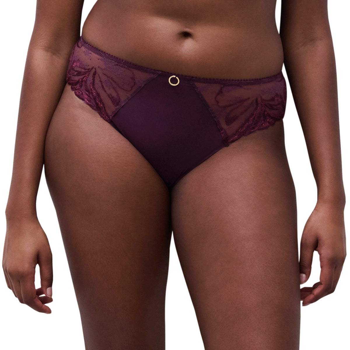 A close-up of a model wearing a pair of low-rise, deep purple lace and mesh panties with a small gold ring detail at the center front.