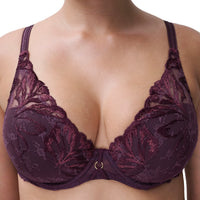 A close-up of a woman wearing a dark plum lace bra with floral embroidery and a small gold ring at the center gore.