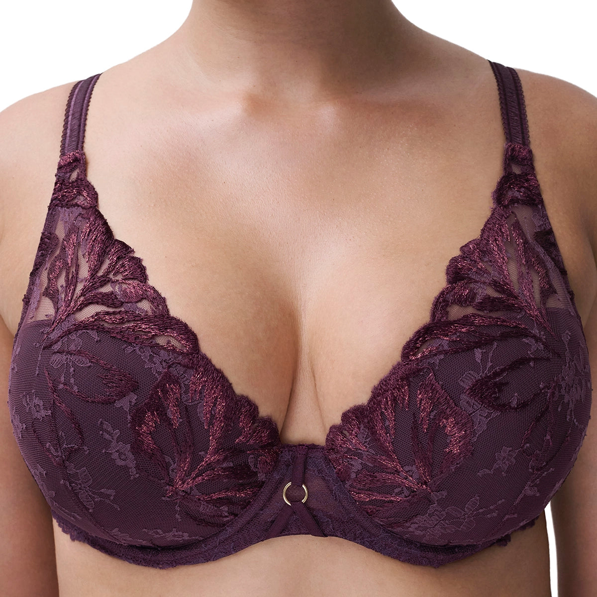 A close-up of a woman wearing a dark plum lace bra with floral embroidery and a small gold ring at the center gore.
