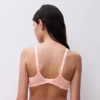 woman wearing a light pink bra against a plain background