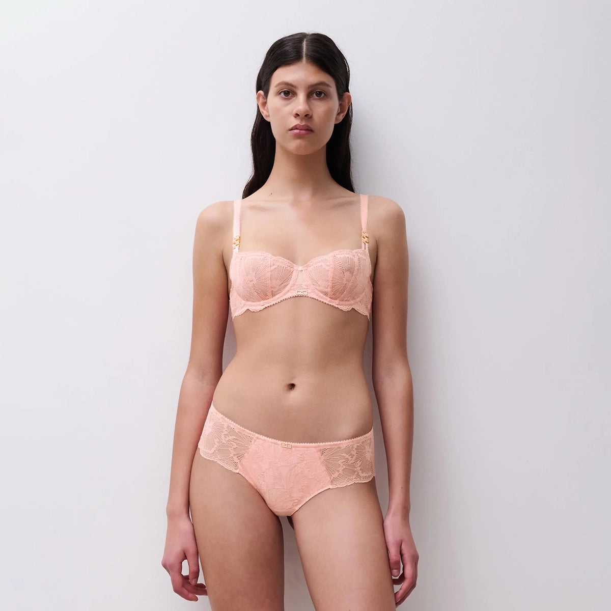 woman wearing a pink lace lingerie set against a plain background