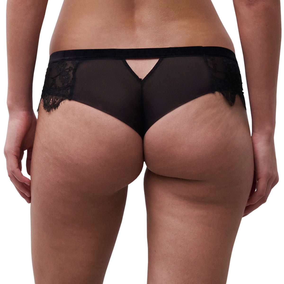 Rear view of a model wearing black lace and sheer mesh panties with a small cutout at the center back, shown against a plain white background.