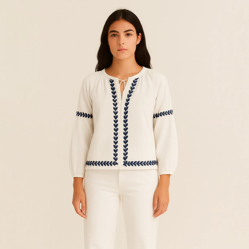 woman wearing a white blouse with blue embroidery on a beige background