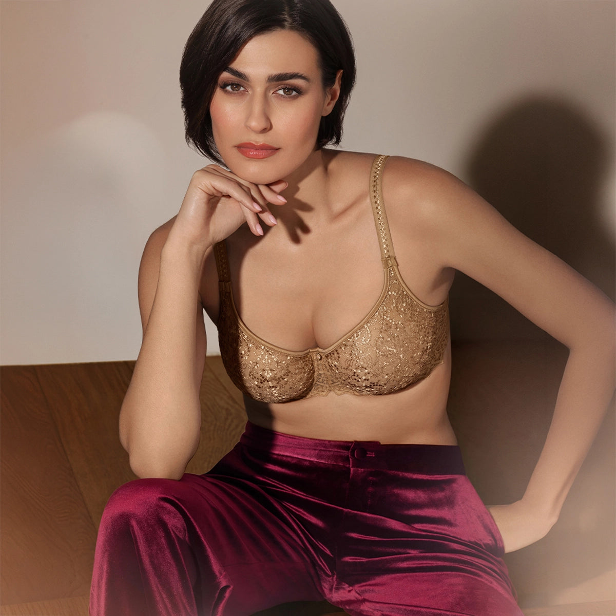 woman wearing a gold bralette and maroon pants against a neutral background