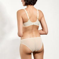 rear view of a model wearing a light beige bra and matching underwear against a plain light background.