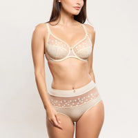 a woman modeling a matching beige lingerie set with a sheer floral lace bra and high-waisted briefs against a plain light background.