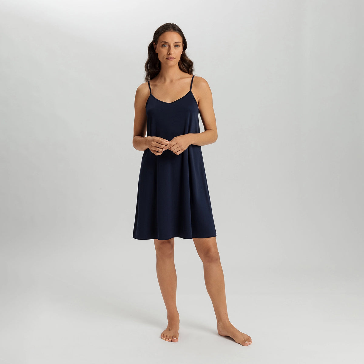A woman modeling a navy blue slip-on camisole nightgown against a light gray studio background.