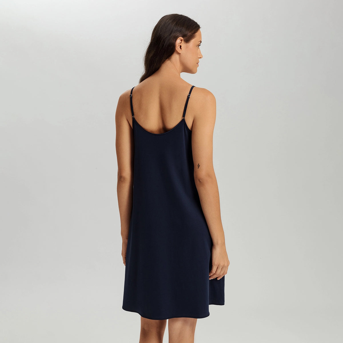 A woman shown from the back wearing a navy blue slip dress with thin straps, photographed against a light gray studio background.