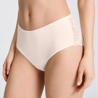 A close-up of a model wearing high-waisted light beige underwear with lace side panels, shown against a plain light gray studio background.