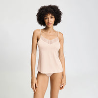 A woman modeling a light peach-pink camisole with a lace V-neckline, paired with matching underwear, against a plain light gray studio background.