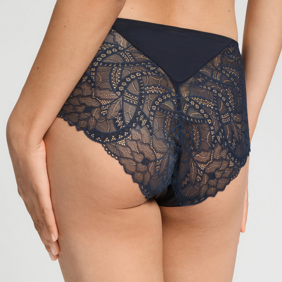 Rear view of a model wearing high-waisted navy lace panties with a solid navy waistband, set against a plain light gray studio background.