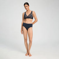 A woman modeling a two-piece lingerie set consisting of a navy blue lace bra and matching solid navy briefs, photographed against a seamless light gray studio background.