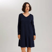 A woman modeling a long-sleeve V-neck shift dress in dark navy blue against a light gray studio background.
