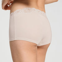 Rear view of a model wearing high-waisted, light beige briefs with a delicate white lace waistband, set against a plain light gray background.