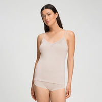 A woman modeling a light beige camisole top with delicate lace trim at the neckline, paired with matching high-waisted briefs, against a plain light gray studio background.