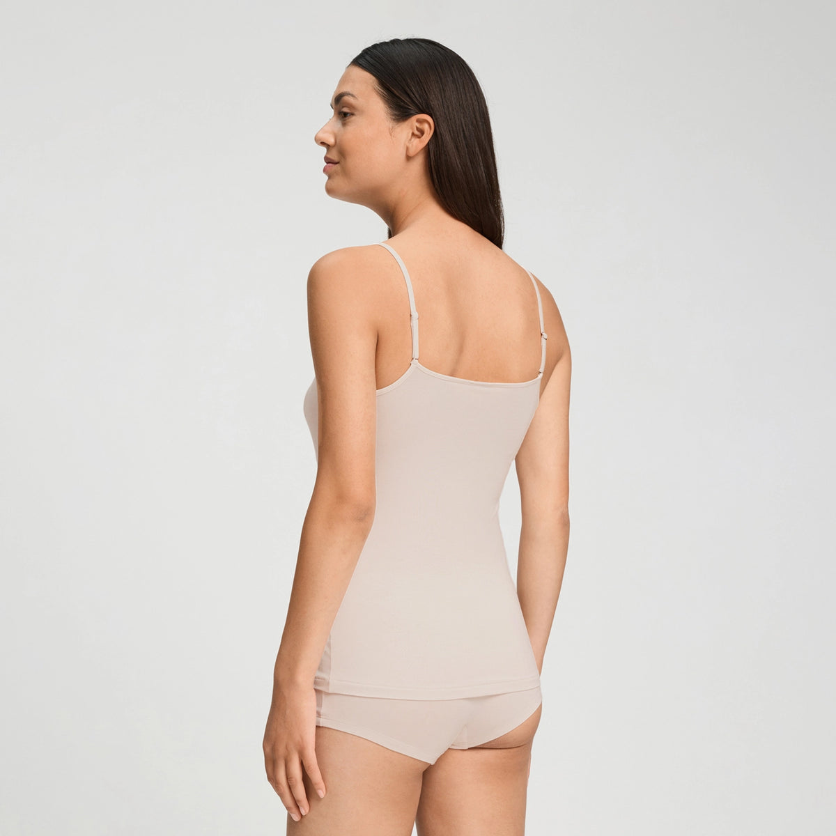 A woman shown from the back wearing a light beige camisole and matching underwear against a plain light gray studio background.