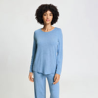 A woman modeling a light blue long-sleeve top and matching pants set against a plain light gray studio background.