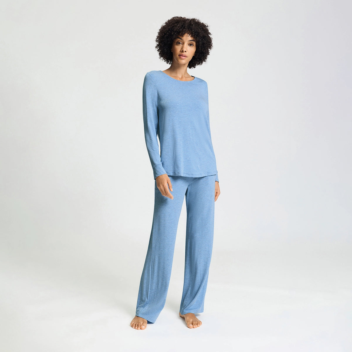 A woman modeling a light blue two-piece pajama set consisting of a long-sleeve top and matching wide-leg pants, photographed against a seamless white studio background.