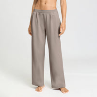 A model wearing wide-leg lounge pants in a taupe-gray color, standing barefoot against a clean white studio background.