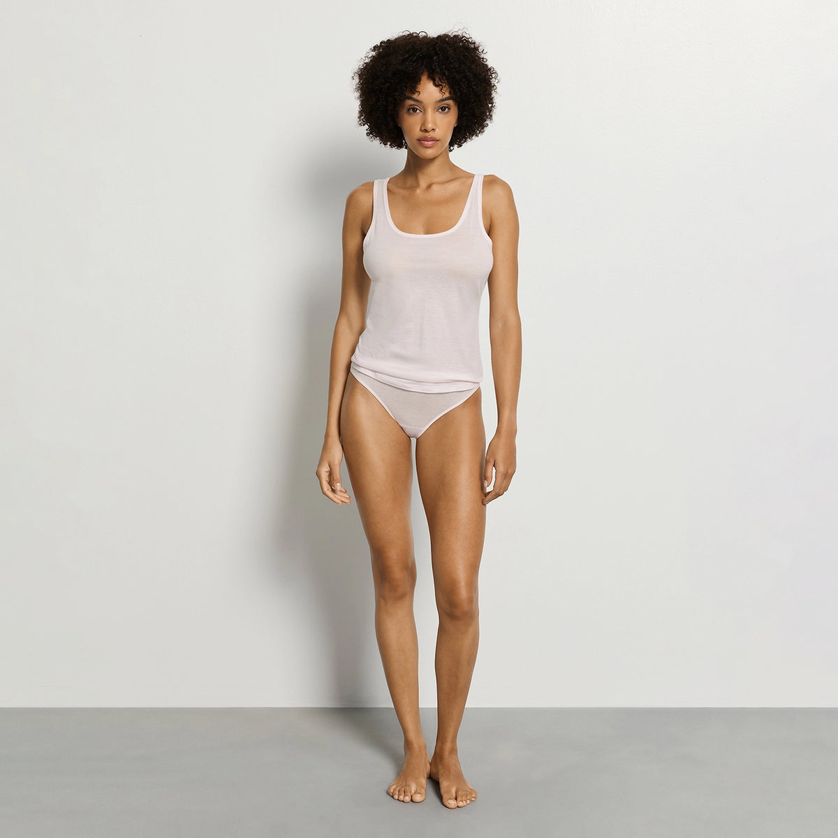 woman wearing a white tank top and beige underwear on a plain background